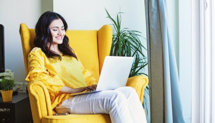 A girl sitting on yellow sofa and working on laptop